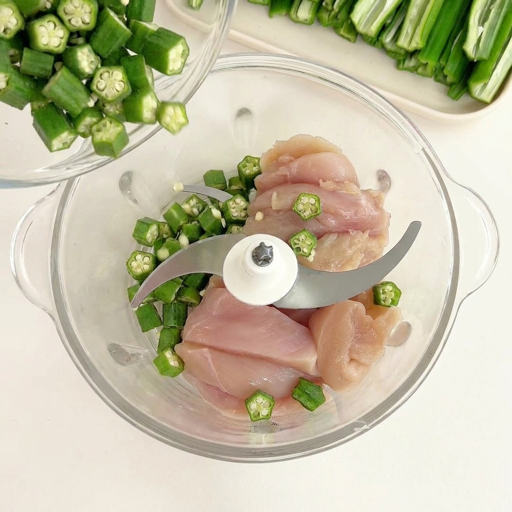 フードプロセッサーの中の鶏肉の上に、取り分けておいたオクラの種を振りかけている様子。