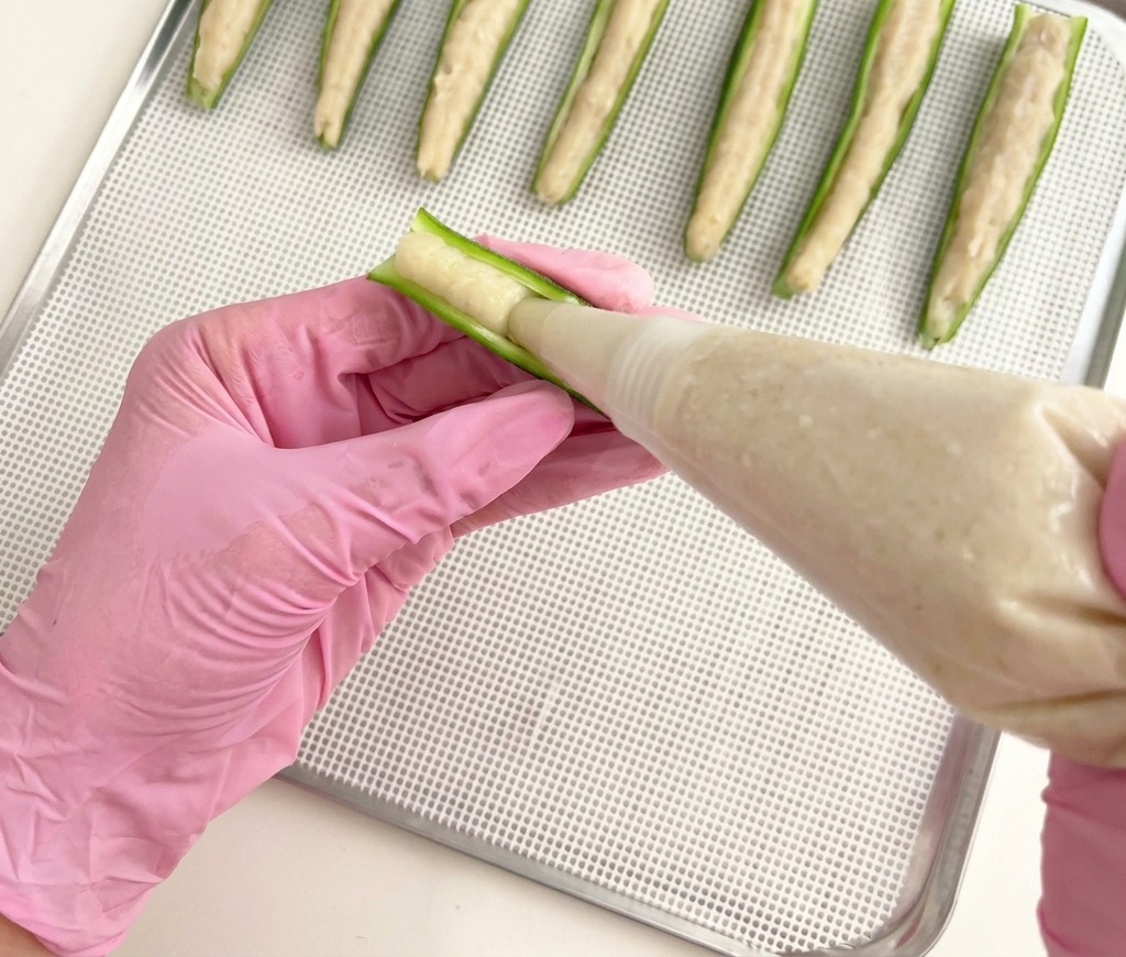 乾燥用のトレイの上で、半分に切ったオクラに鶏肉ペーストを丁寧に絞り出している様子。