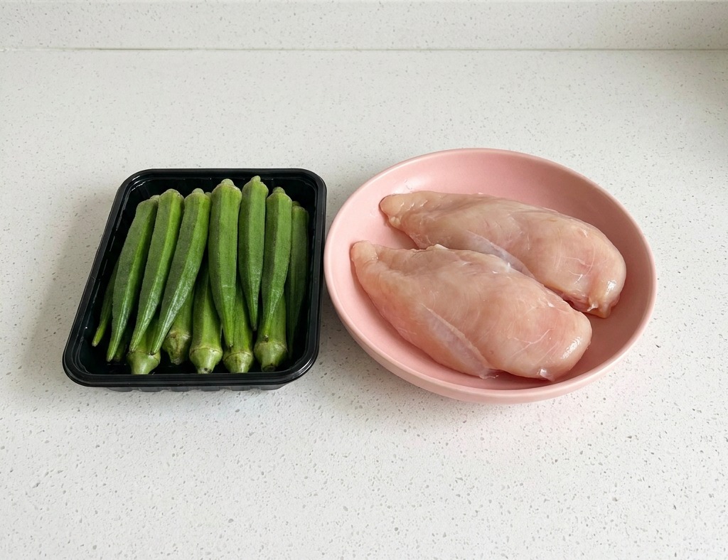 黒いトレイに乗った新鮮なオクラと、白いカウンターのピンクの皿に乗った鶏むね肉。