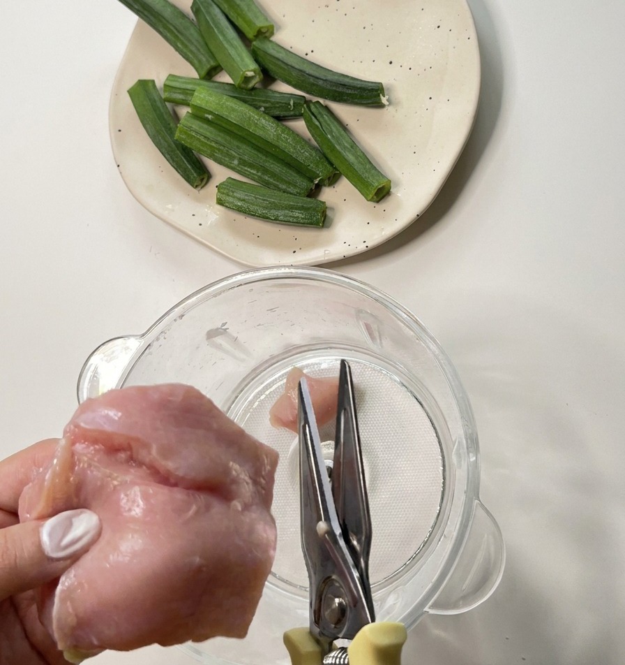 キッチンバサミを使って、生の鶏むね肉をブレンダーの容器の中に小さく切り入れている様子。