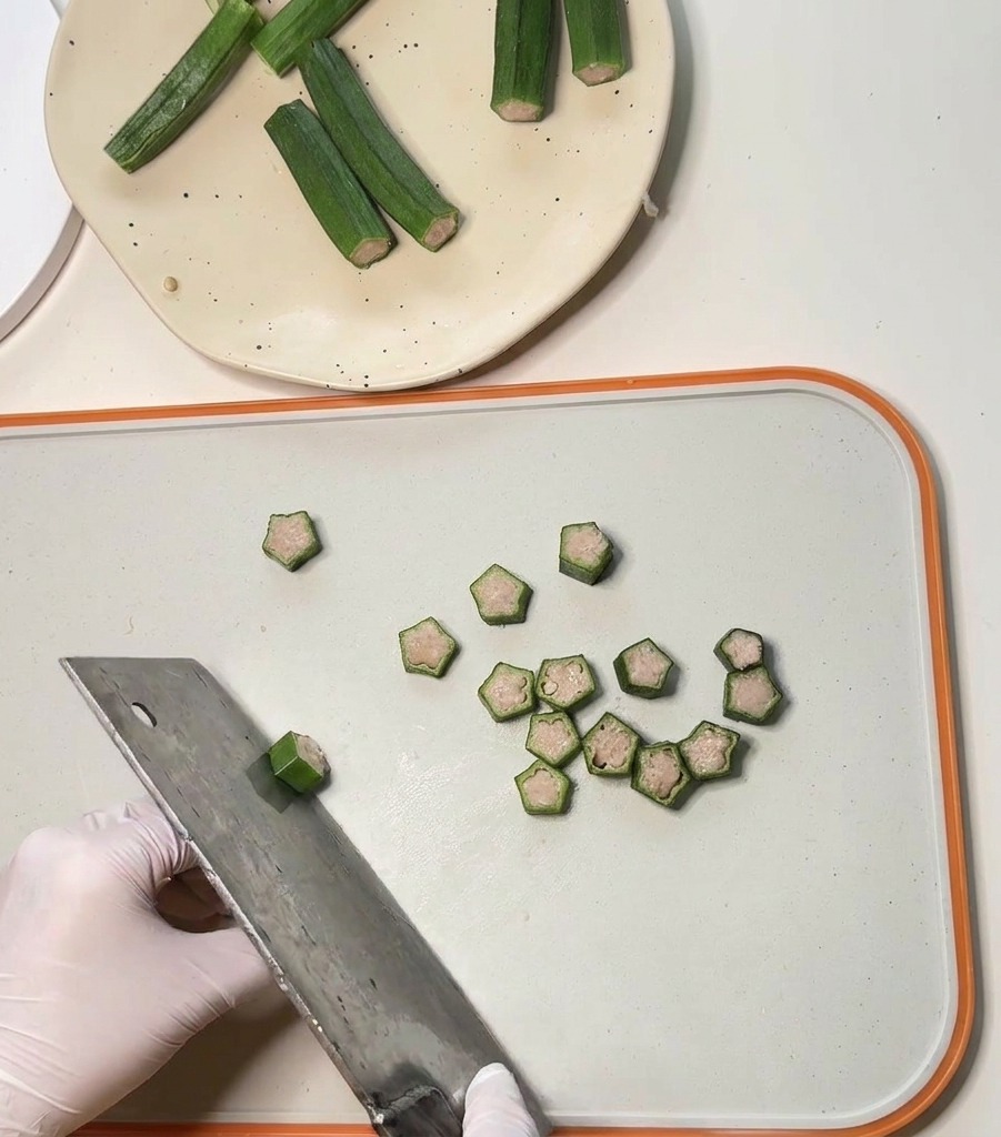 中華包丁を使い、肉を詰めたオクラを小さくスライスして星型のチップスを作っている様子。