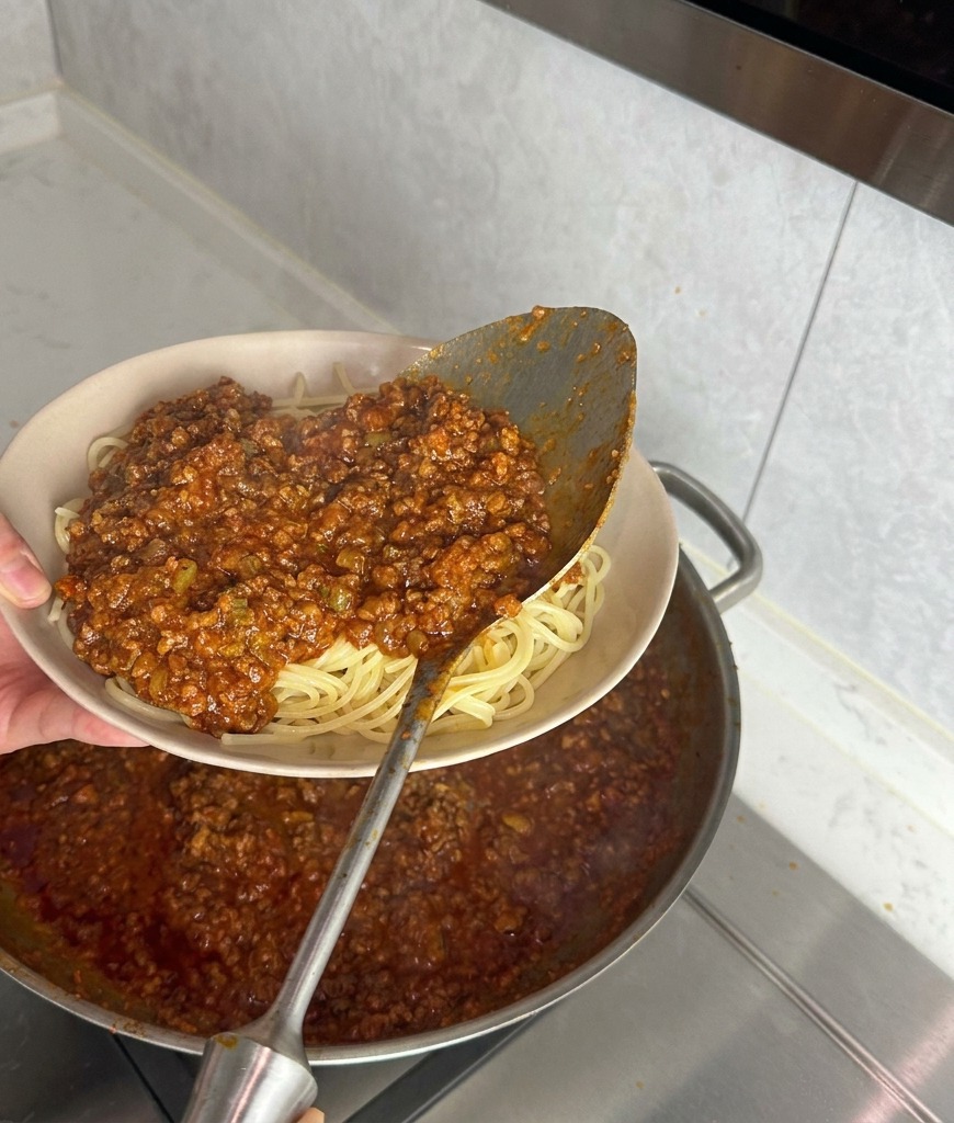 器に盛られたスパゲッティに、お玉でたっぷりと厚みのあるミートソースをかけている様子。