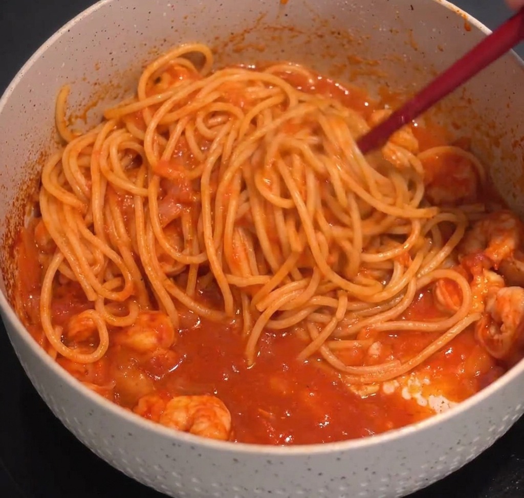 トングでパスタとソースを艶が出るまで混ぜ合わせる様子