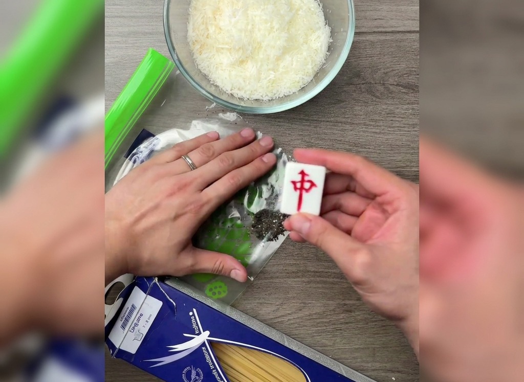 木製のテーブルの上で、ビニール袋に入れた黒胡椒を麻雀牌の平らな面を使って押し潰している様子。