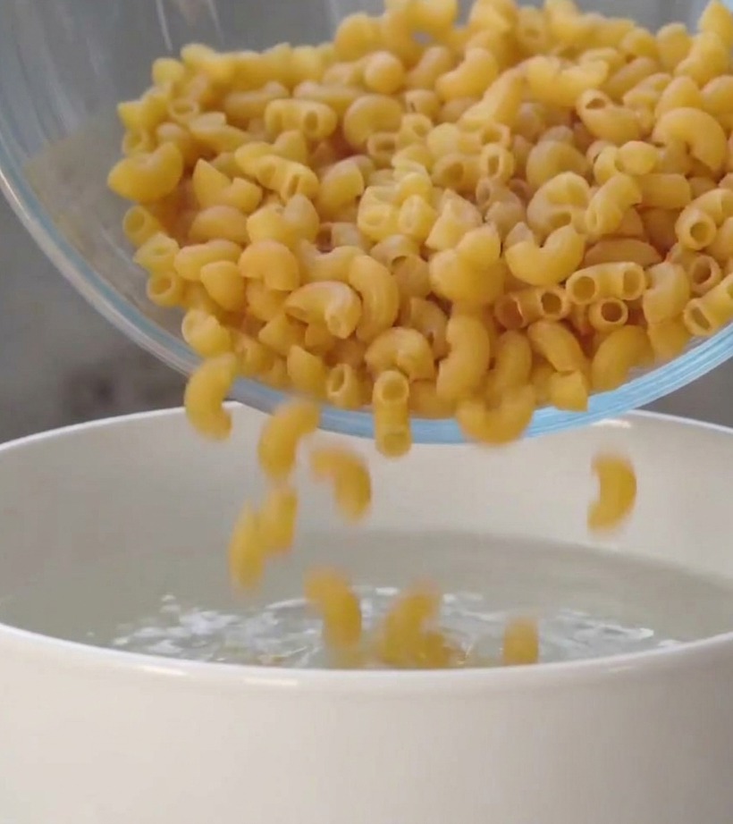 白い鍋の沸騰したお湯に、ガラスボウルから乾いたスパイラルパスタを入れている様子