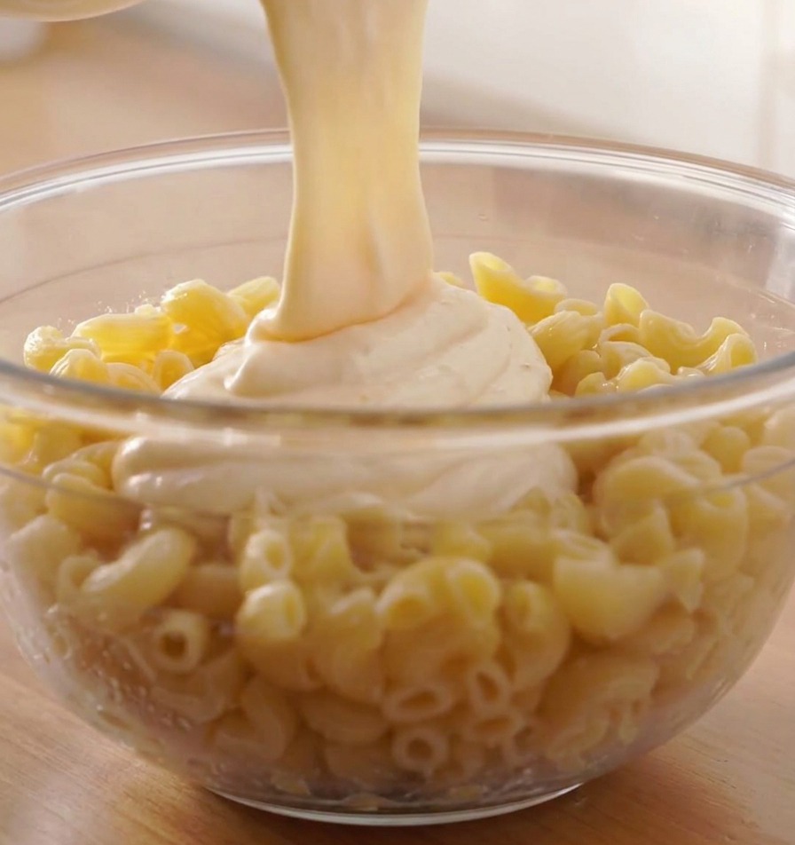 茹で上がったスパイラルパスタが入った大きなボウルに、熱々のチーズソースを注いでいる様子
