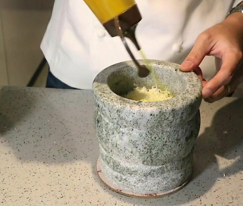 すり鉢の中の材料に黄金色のオリーブオイルを注いでいる様子。