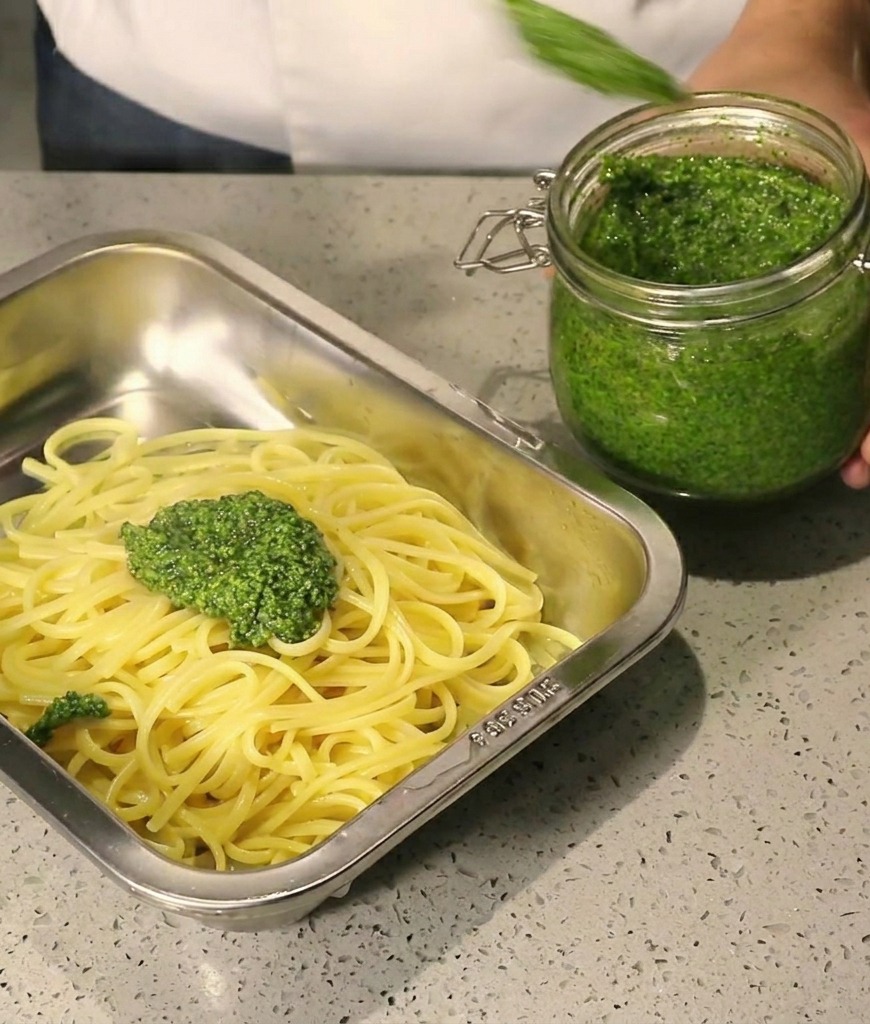 熱いパスタの上に手作りバジルペーストをのせている様子。