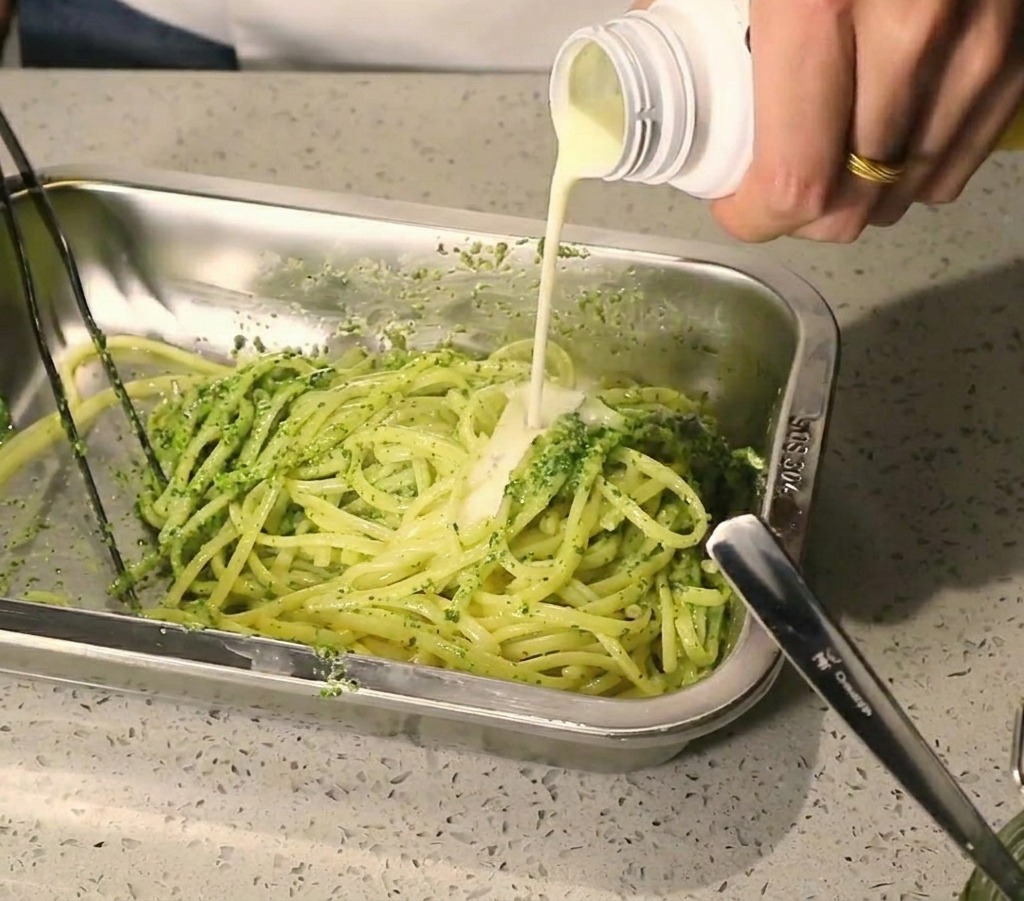 ペーストがのったパスタに白いクリームソースを注いでいる様子。