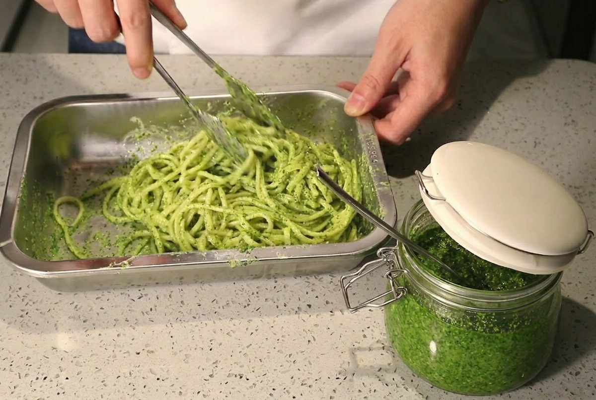 トングでパスタ、ペースト、クリームを混ぜ合わせている様子。