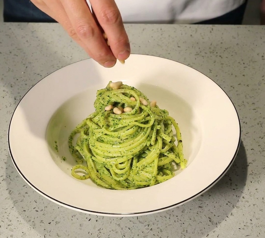 皿に盛り付けたジェノベーゼパスタの上に松の実をトッピングしている様子。