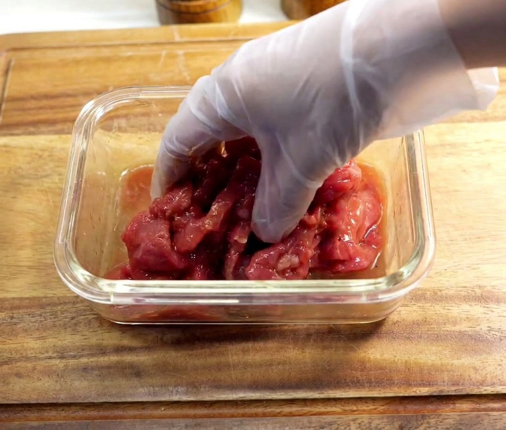 手袋をはめた手で、ボウルの中の牛肉と調味料をしっかりと揉み込んでいる様子