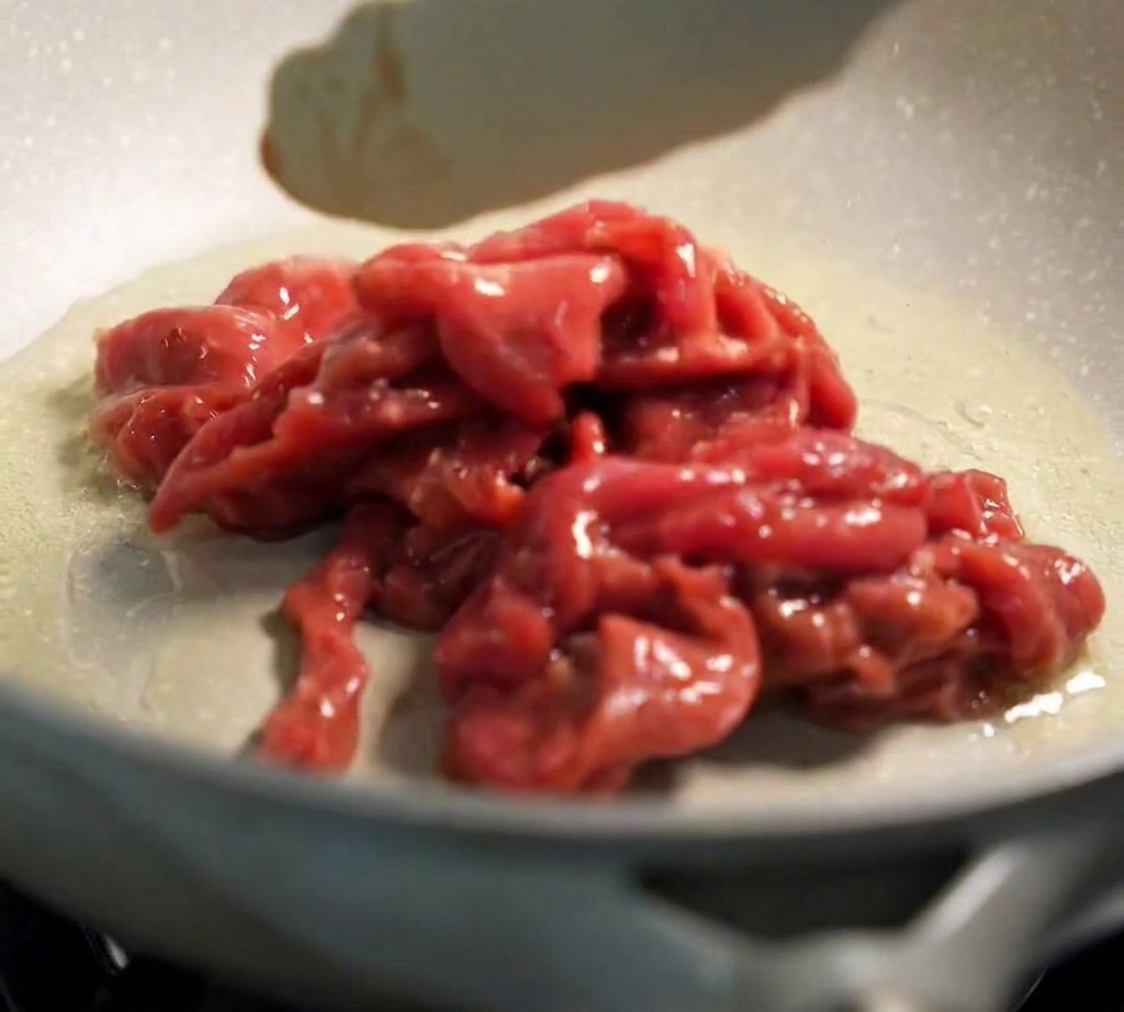 熱したフライパンにトングで牛肉を並べ、強火で焼いている様子