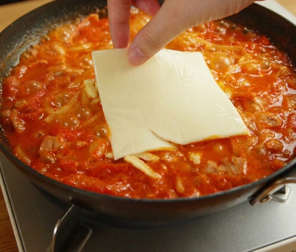 溶けかけたチーズとうどんの上に、黄色いスライスチーズをのせている様子。