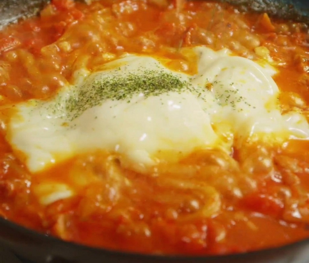 溶けた2色のチーズがのったうどんの上に、緑色のハーブパウダーを散らしている様子。
