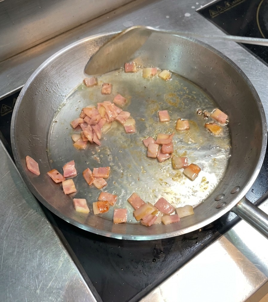 フライパンの中でベーコンがジューシーに色づき、ヘラで混ぜながら炒められている様子。