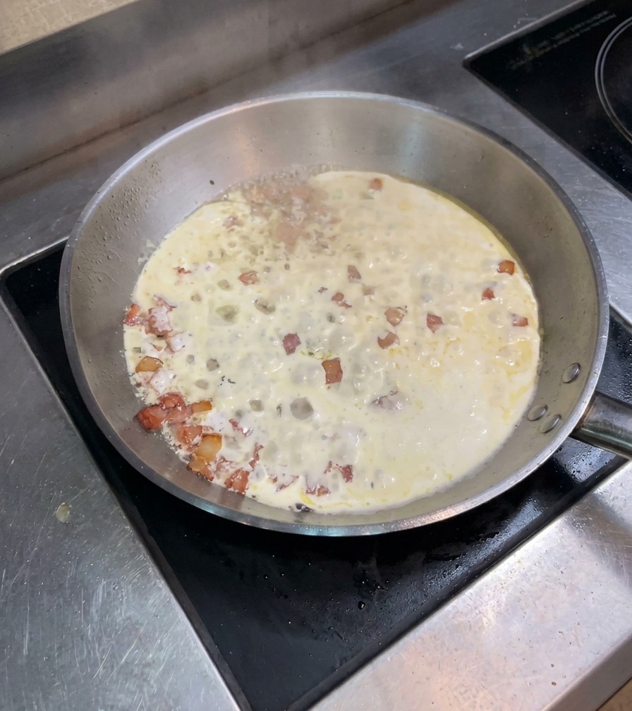 フライパンの中で生クリームとベーコンが泡立ちながら煮詰まっている様子。
