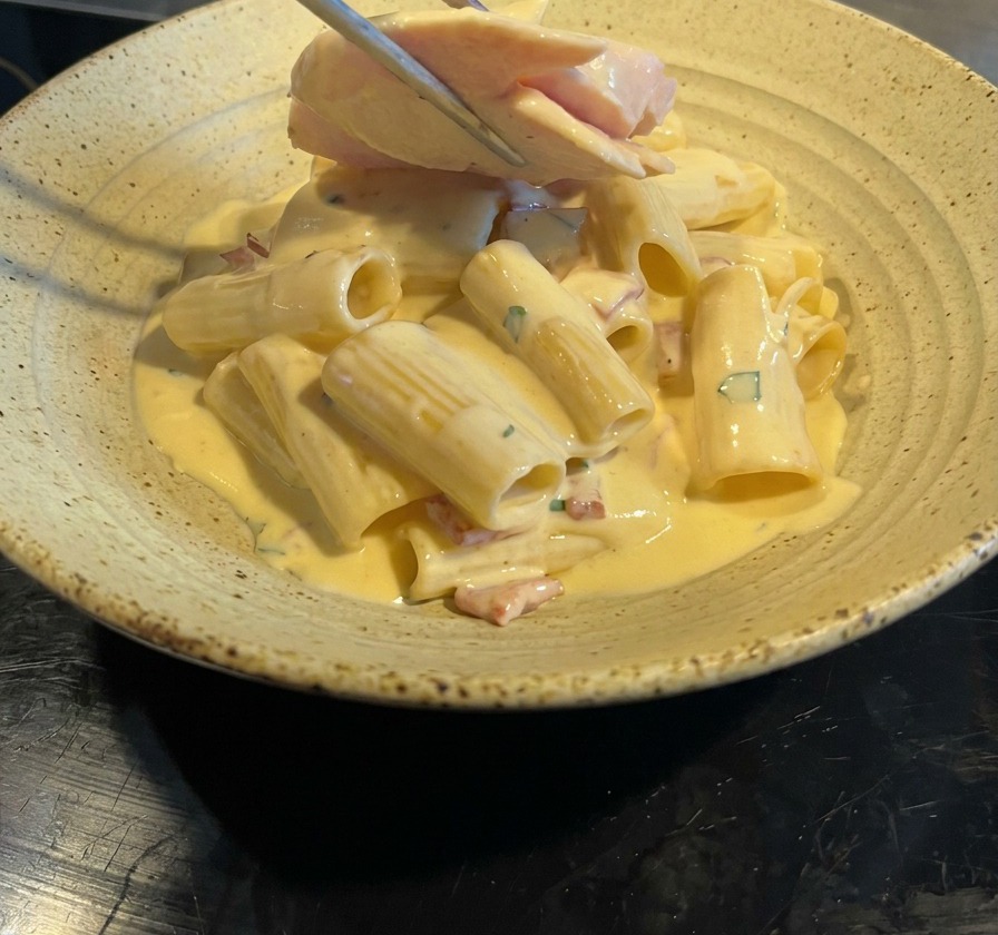 盛り付けたパスタの上に、トングでスライスした鶏むね肉を乗せている様子。