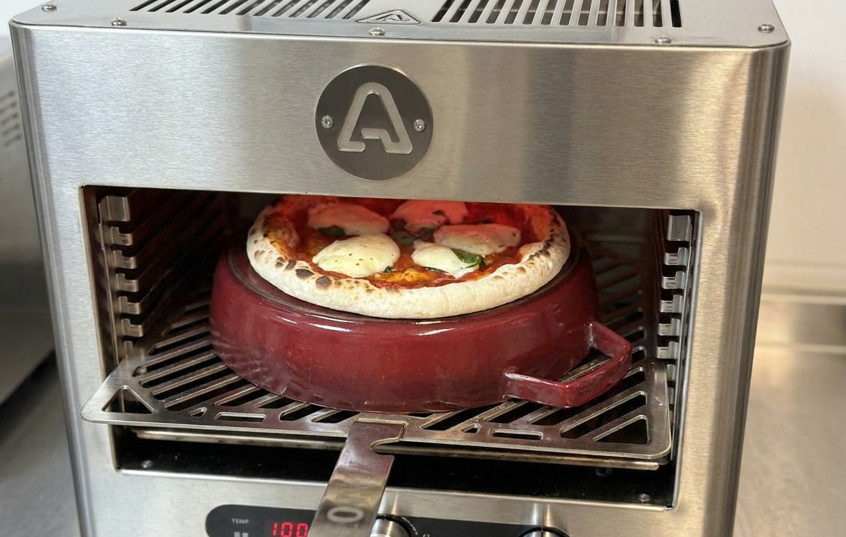 金属製のピザピールを差し込み、鋳鉄鍋の上で焼き上がりに近いピザを回転させている様子。
