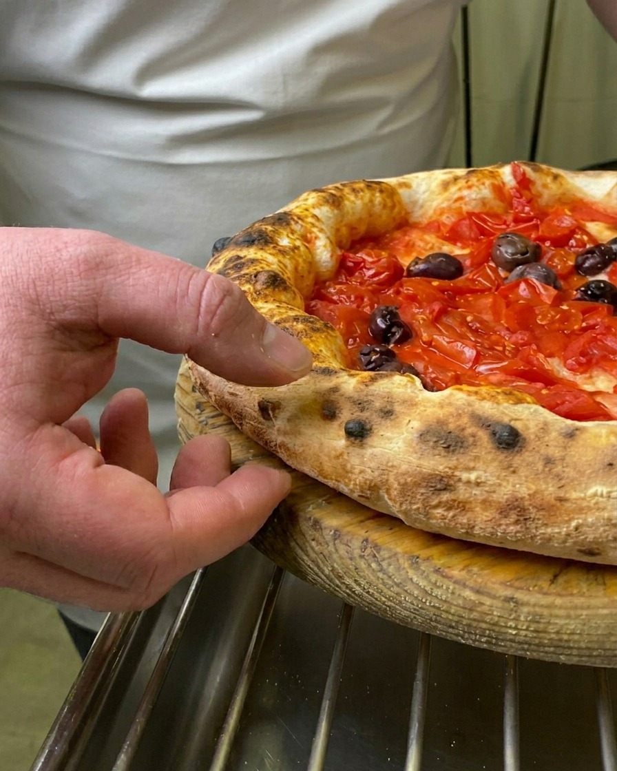 焼き立てのマリナーラピッツァの、ふっくらと焦げ目のついた縁を指で押して確認する様子