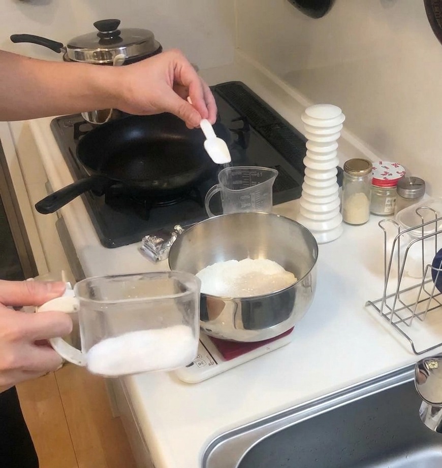 キッチンスケールに乗ったボウルの中で、小麦粉とイーストに砂糖を合わせている様子。