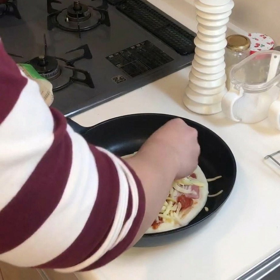 具材がのったピザの上に、シュレッドチーズを山盛りに振りかけている様子。