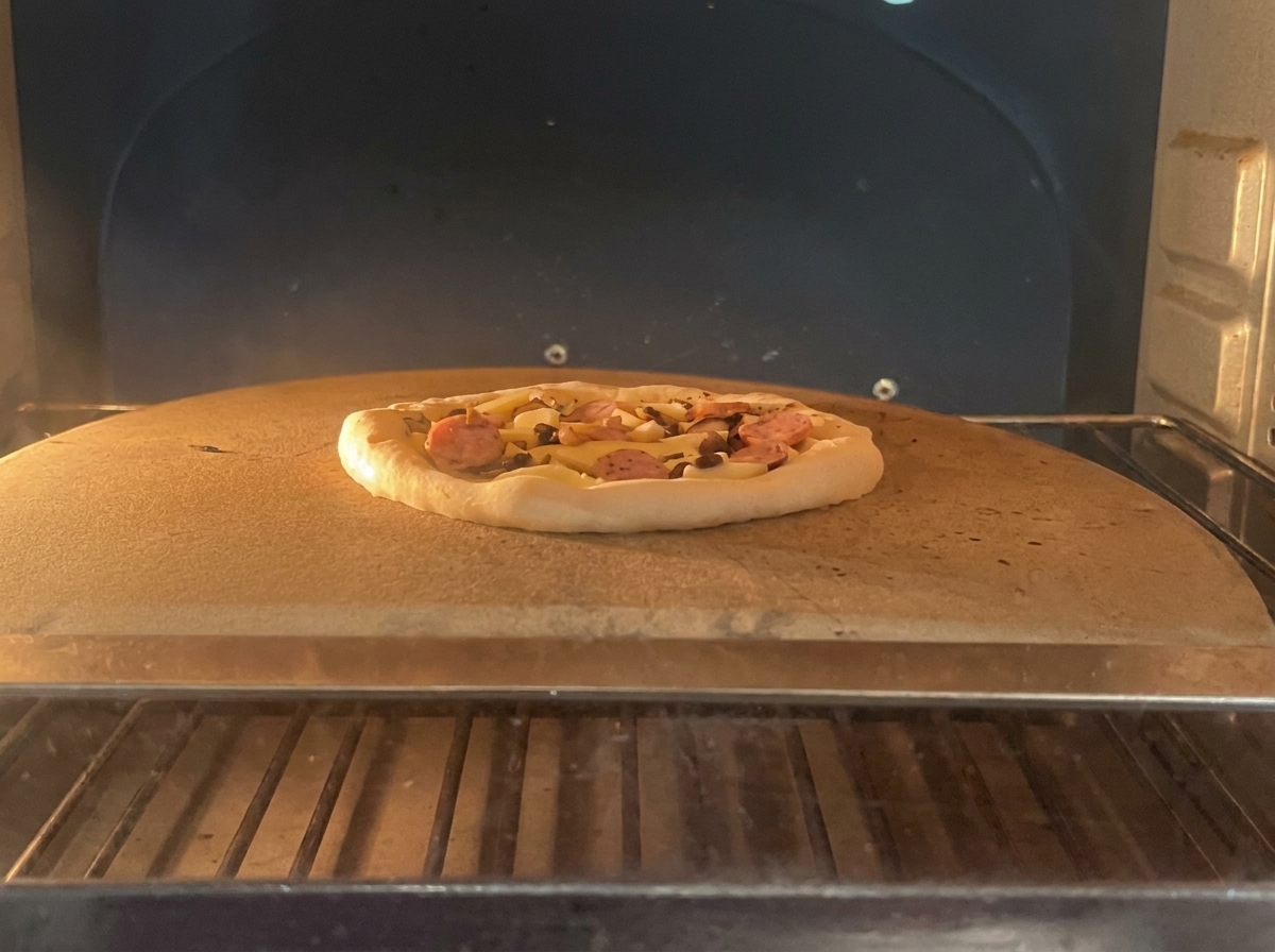 ペパロニとキノコを乗せたピザを、専門的なオーブン内のピザストーンに乗せている様子。