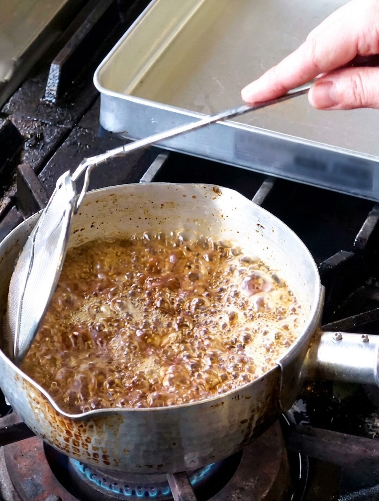 鍋の中で勢いよく泡立ち、湯気が立ち上りながら揚がっているにんにくの様子。