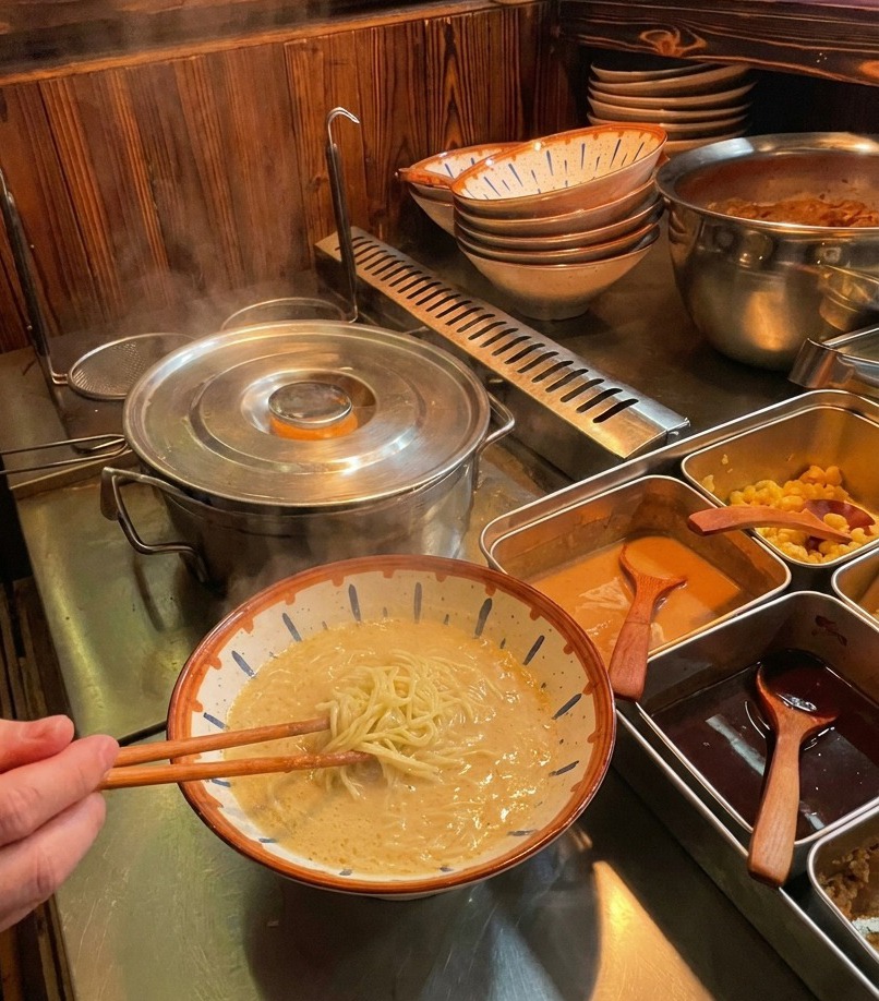 箸を使ってスープの中で麺をきれいに折り畳み、盛り付けの土台を作っている様子。
