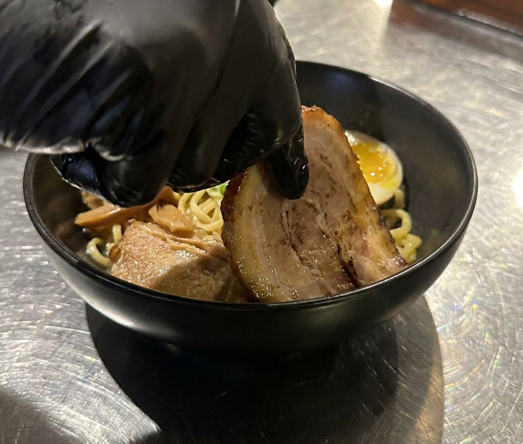 麺と卵が盛られた器の脇に、厚切りのチャーシューを丁寧に添えている手元のアップ。