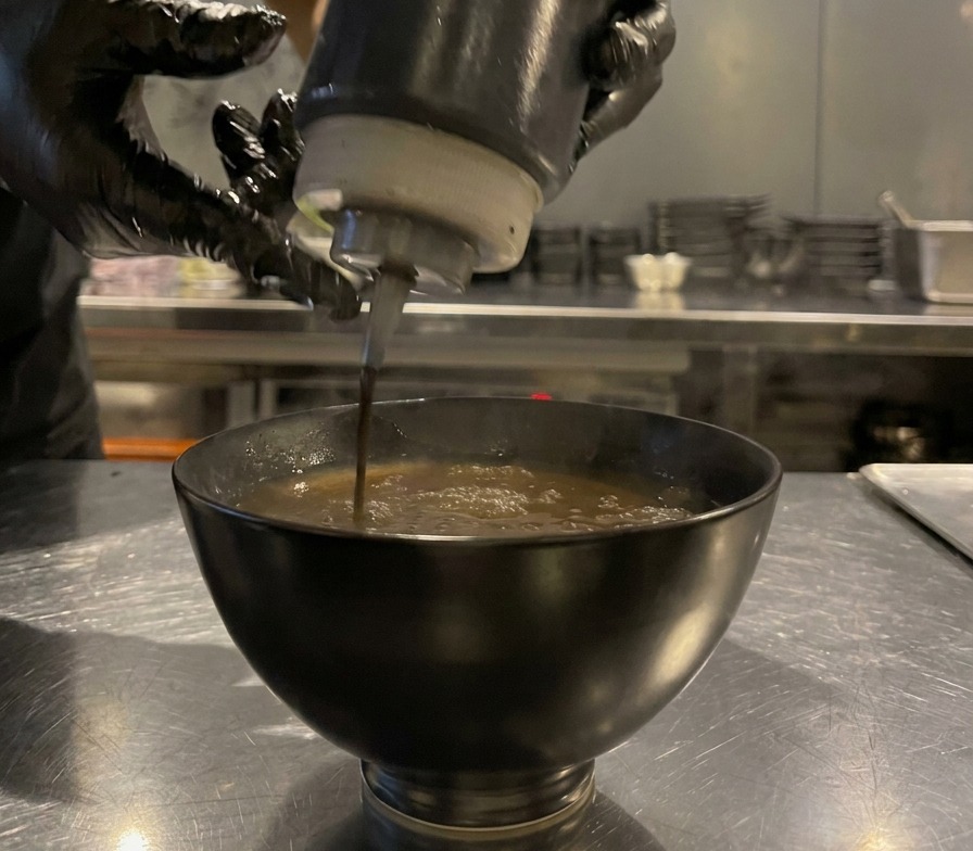 注がれたソースの上に、ボトルから直接黒マー油を数滴垂らして仕上げている様子。