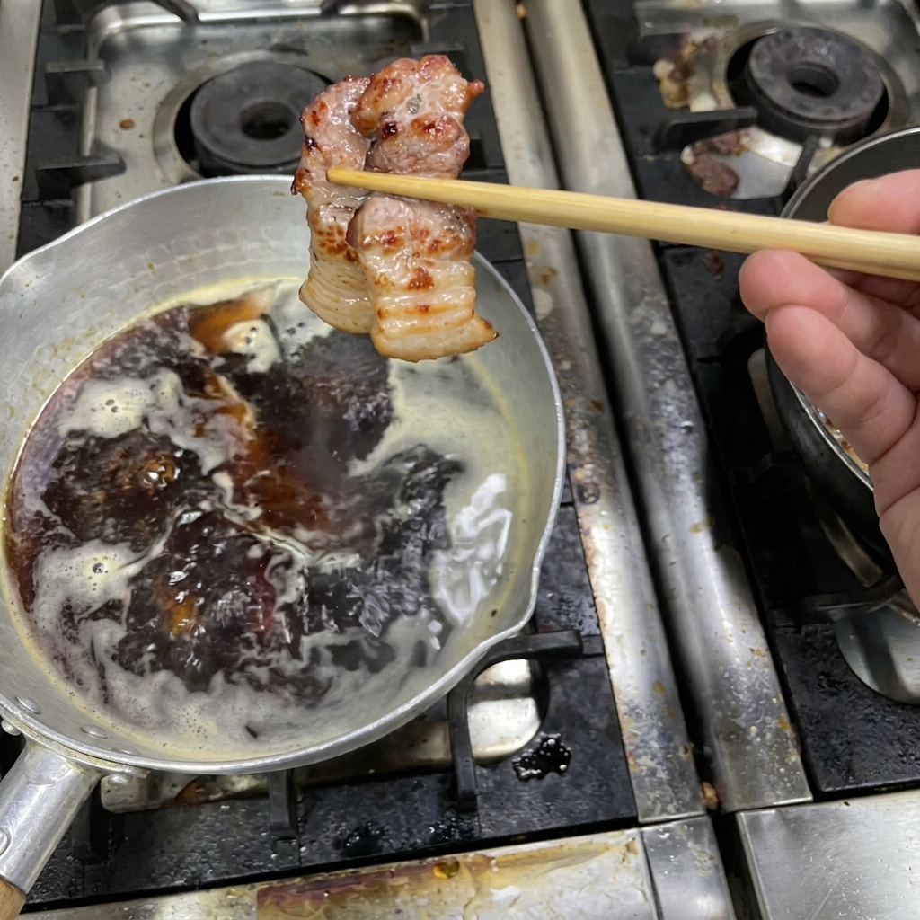 焼き色のついた豚肉を、タレの入った小鍋に移して煮込んでいる様子。
