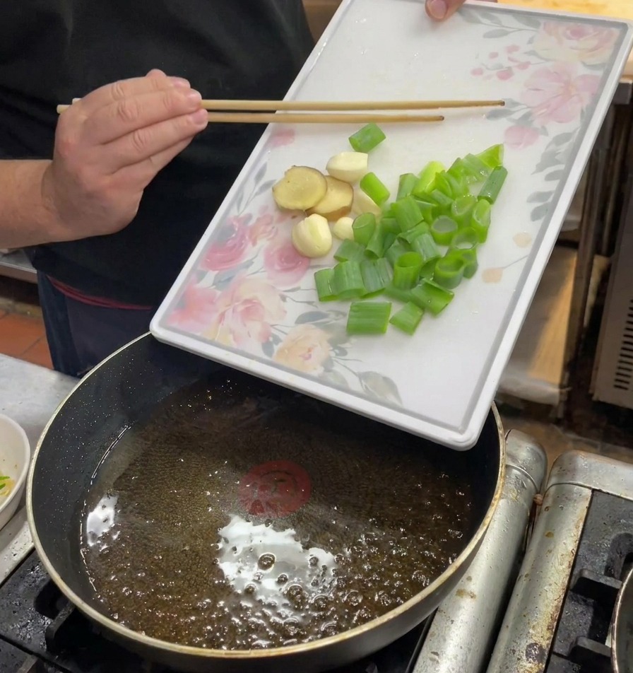 豚の脂が溶け出したオイルに、ねぎ、生姜、にんにくを入れる様子。