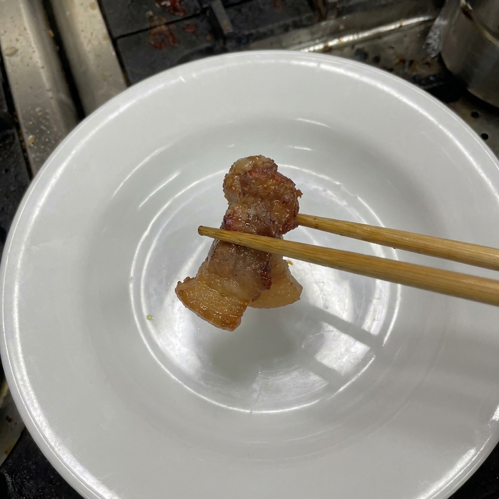箸で柔らかく煮上がった豚肉を皿に取り出している様子。