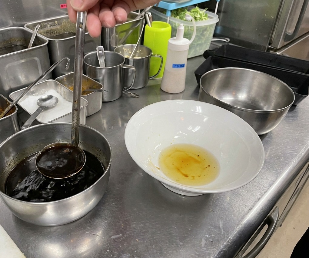 油の入った器に、さらに煮詰まった濃厚なタレを加えている様子。