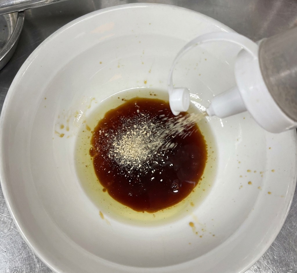 器の中のタレに、すりごまと黒胡椒を振りかけている様子。