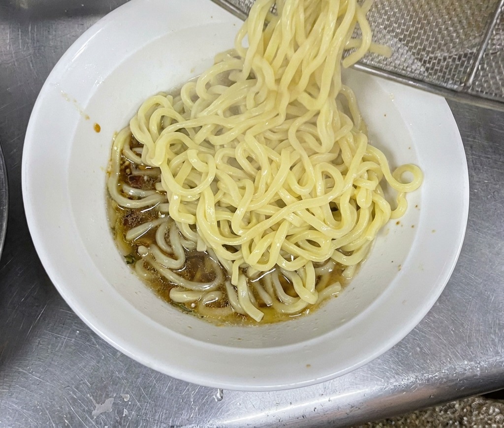 茹でたての熱々な太麺を器に入れ、タレと混ぜ合わせている様子。