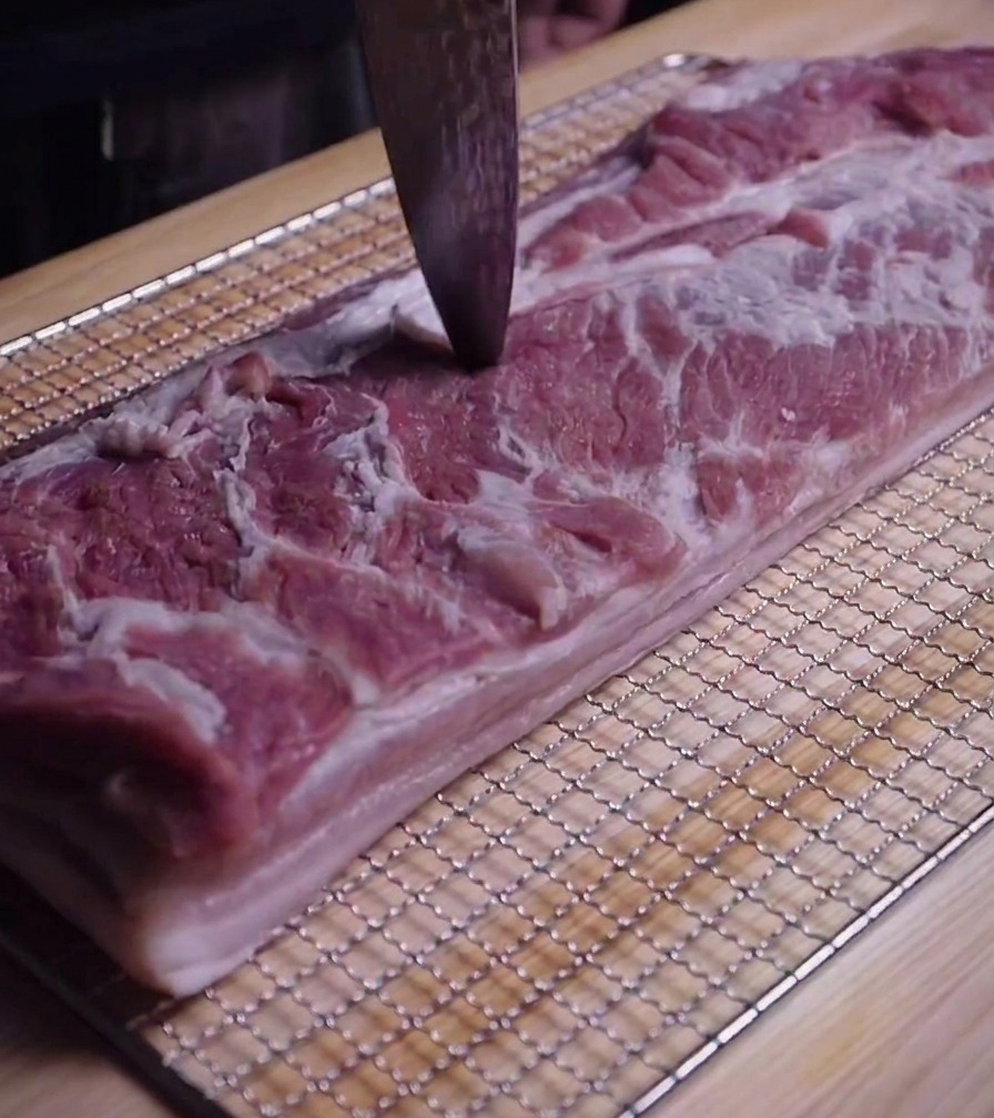 包丁の先で豚バラ肉の表面に細かな穴を開けている様子。