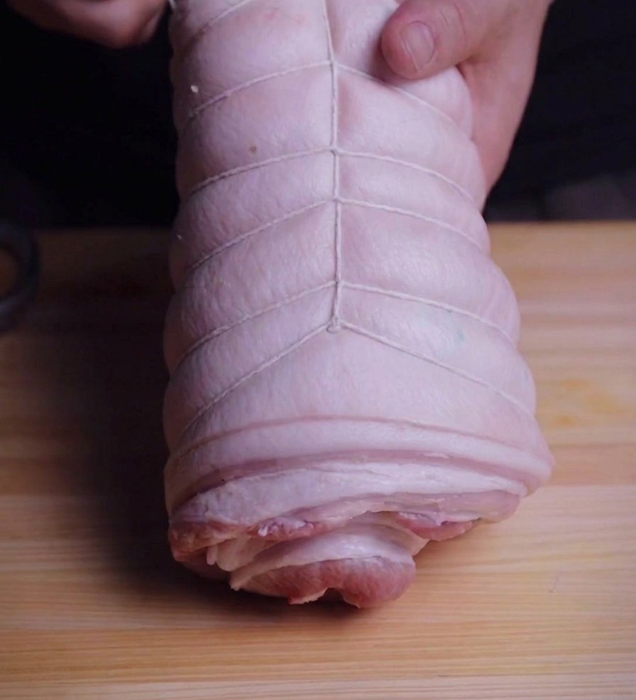 タコ糸を使って、円筒状に巻いた豚肉をしっかりと縛っている様子。