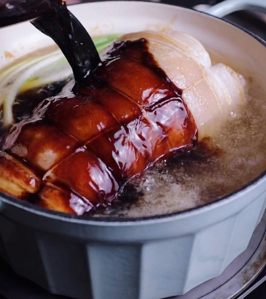 鍋に入れた肉と長ねぎの上から、計量カップに入れた濃い色の煮汁を注いでいる様子。