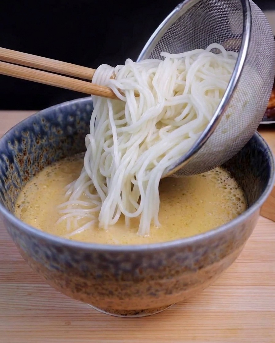 湯切りした麺を、黄色い豚骨スープが入った器に入れている様子。