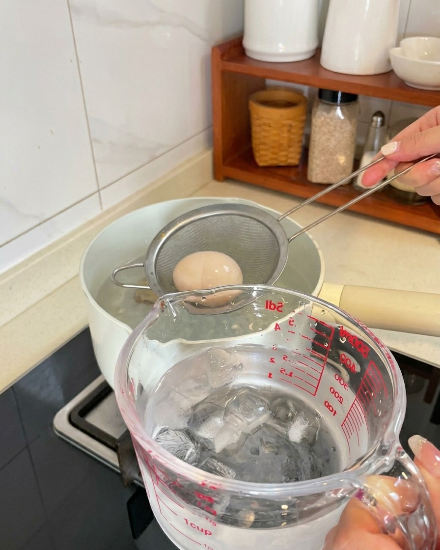 茹で上がった卵を網じゃくしですくい、氷水の入った容器に移している様子。