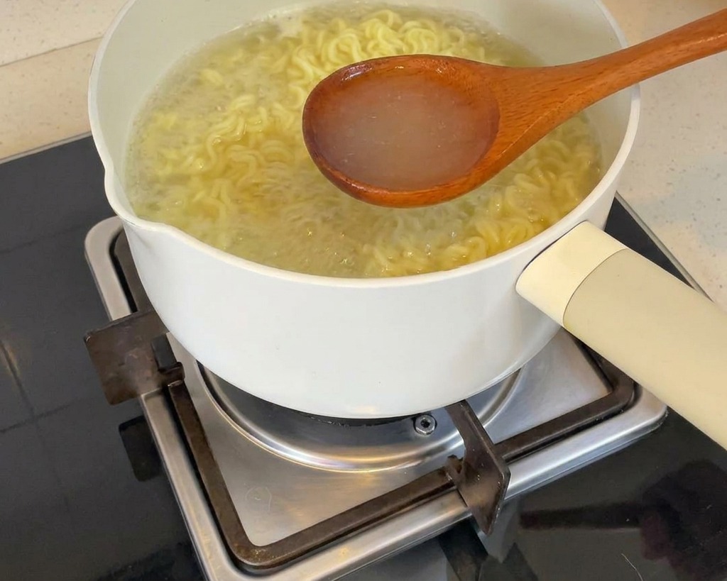 鍋から熱々のゆで汁をお玉ですくい上げている様子。
