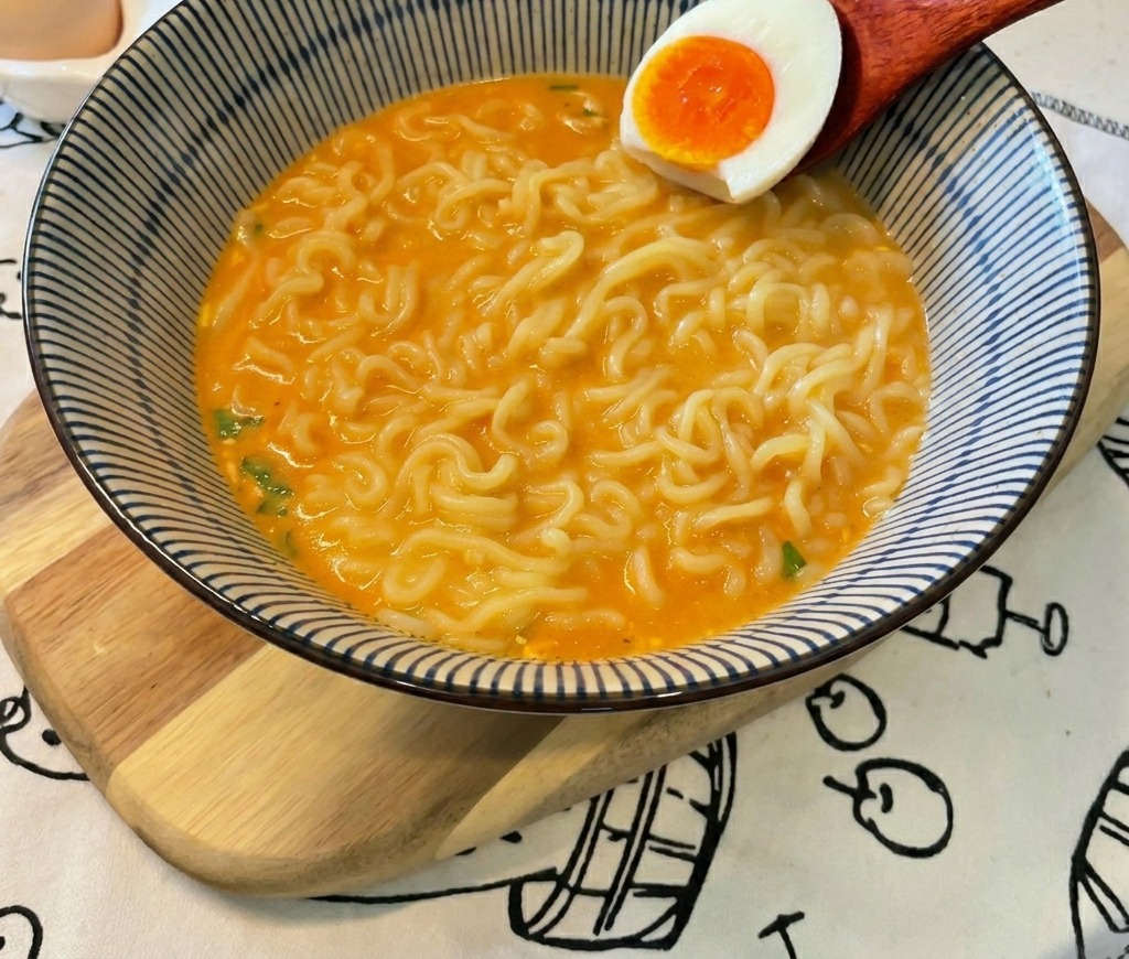 半分に切った、黄身がとろとろの卵をラーメンの上にのせている様子。
