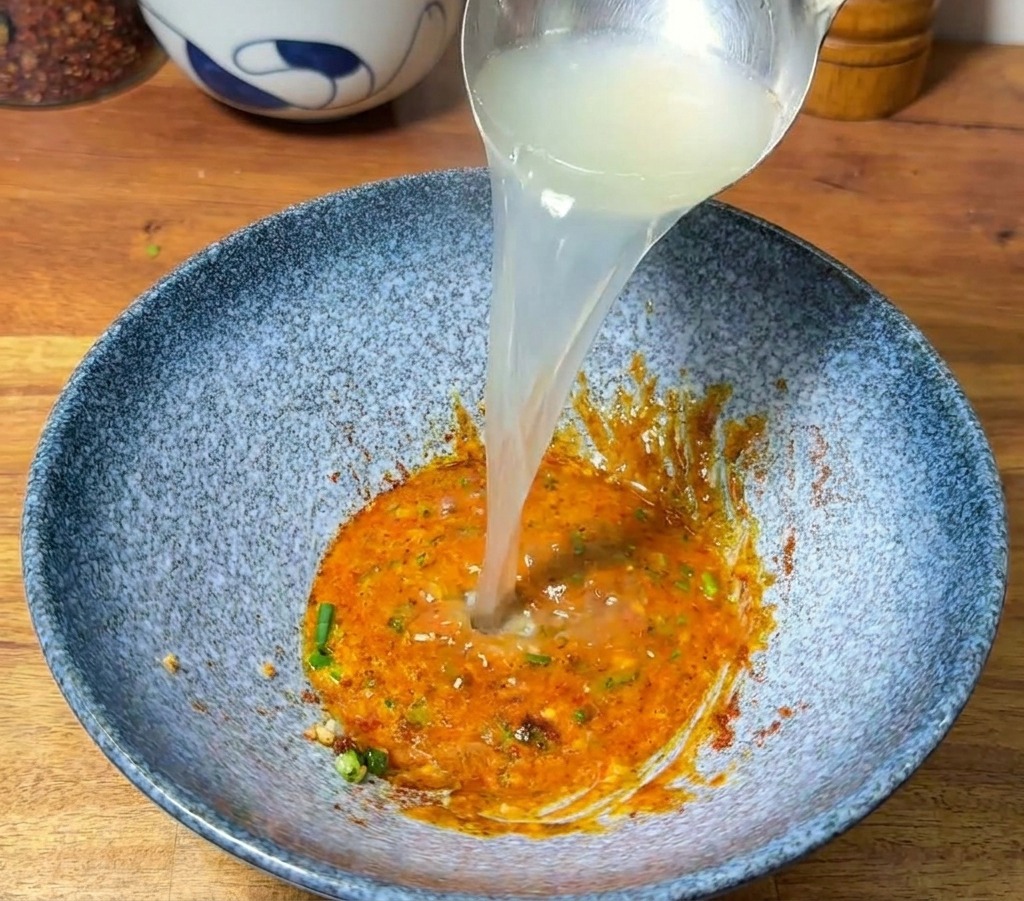 ペーストが入った器に、おたまを使って熱々の茹で汁を注いでいる様子。
