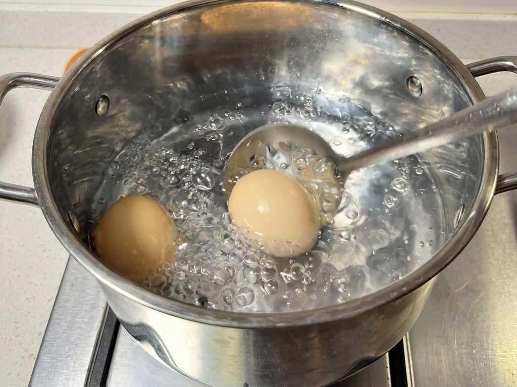 沸騰したお湯から、穴あきスプーンで2つの卵をすくい上げている様子。