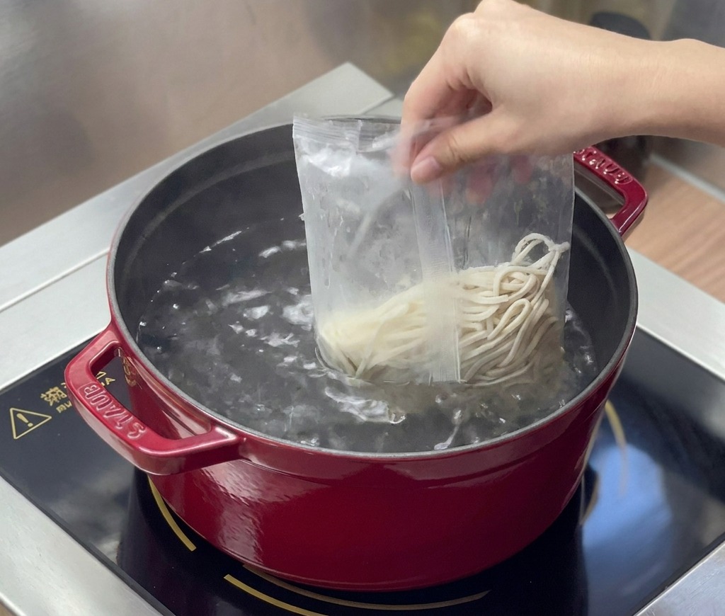 沸騰したお湯が入った鍋に、袋から出した中華麺を入れている様子。