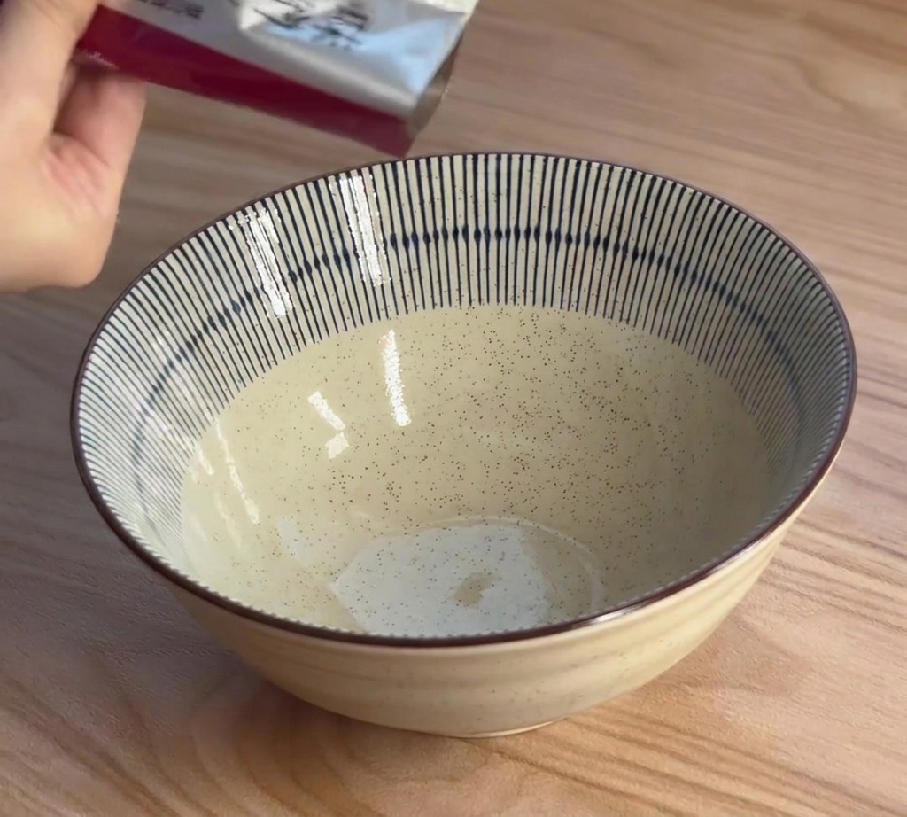 青と白のストライプ柄のラーメン丼に、パックから味噌スープの素を絞り出している様子。