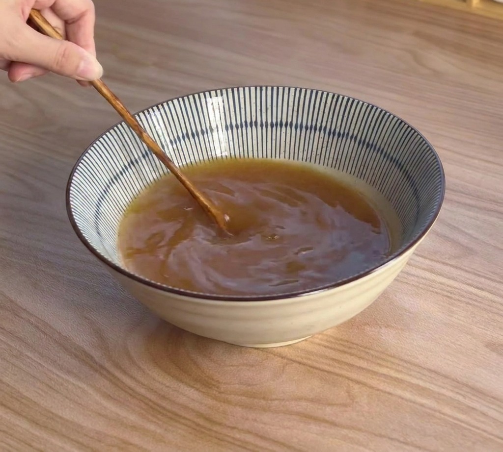 木製のスプーンを使って、丼の中の味噌スープを均一になるまで混ぜている様子。