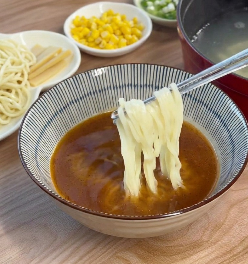 箸で麺を持ち上げ、味噌スープの入った丼の中にバランスよく入れている様子。